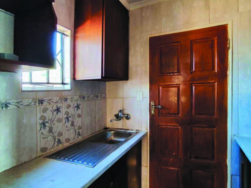A compact scullery or utility area featuring a stainless steel sink, tiled splashback, and built-in cabinetry, providing functional space for food preparation or laundry tasks.