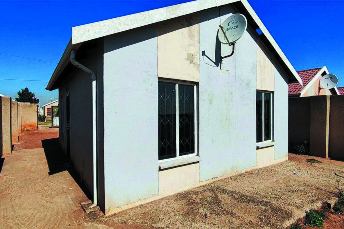 Rear view of a detached house featuring a gable roof, security bars on windows, and a satellite dish mounted on the exterior wall.