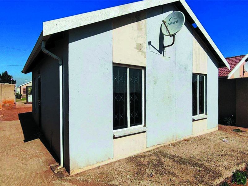 Rear view of a detached house featuring a gable roof, security bars on windows, and a satellite dish mounted on the exterior wall.