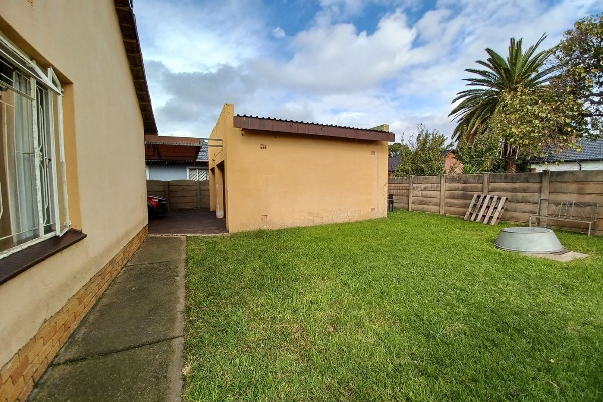Rear garden view featuring a lawn, concrete pathway, and a detached garage with a paved driveway area.