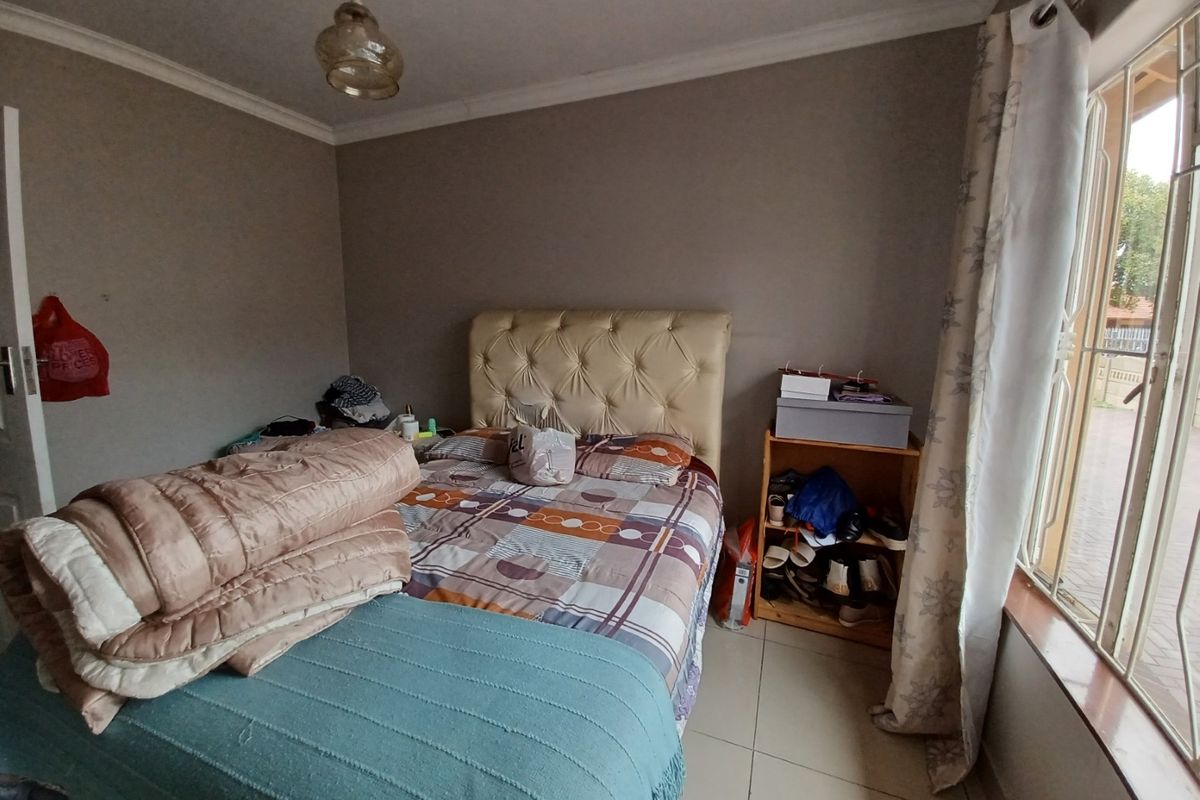 A standard bedroom featuring tiled flooring, coved ceilings, and a large window with security bars, providing natural light.