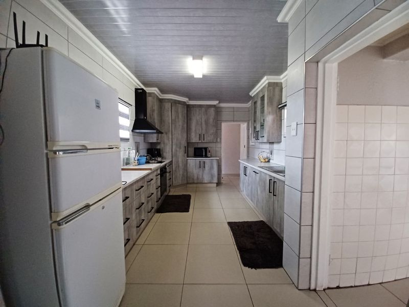 A functional galley-style kitchen featuring grey wood-look cabinetry, tiled walls and flooring, and a modern extractor fan.