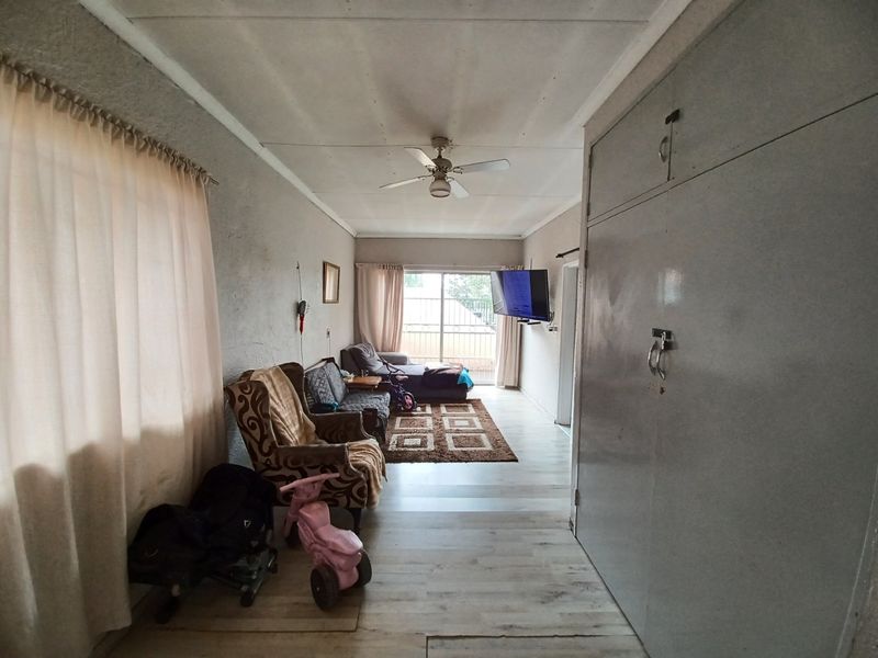 A living room featuring laminate flooring, a ceiling fan, and extensive built-in cupboard storage, with access to an outdoor area via a sliding glass door.