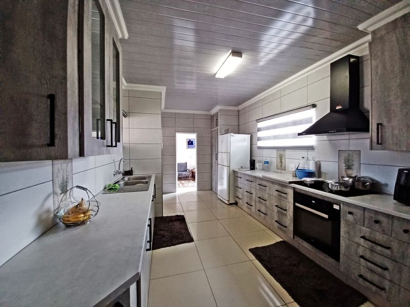 Modern kitchen featuring extensive built-in cabinetry, tiled finishes, integrated oven and hob, and a sleek extractor fan, offering a functional and well-maintained workspace.