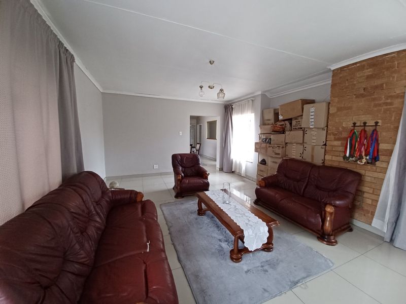 A spacious living room featuring tiled flooring and a prominent exposed brick fireplace, offering a neutral canvas for potential interior updates.