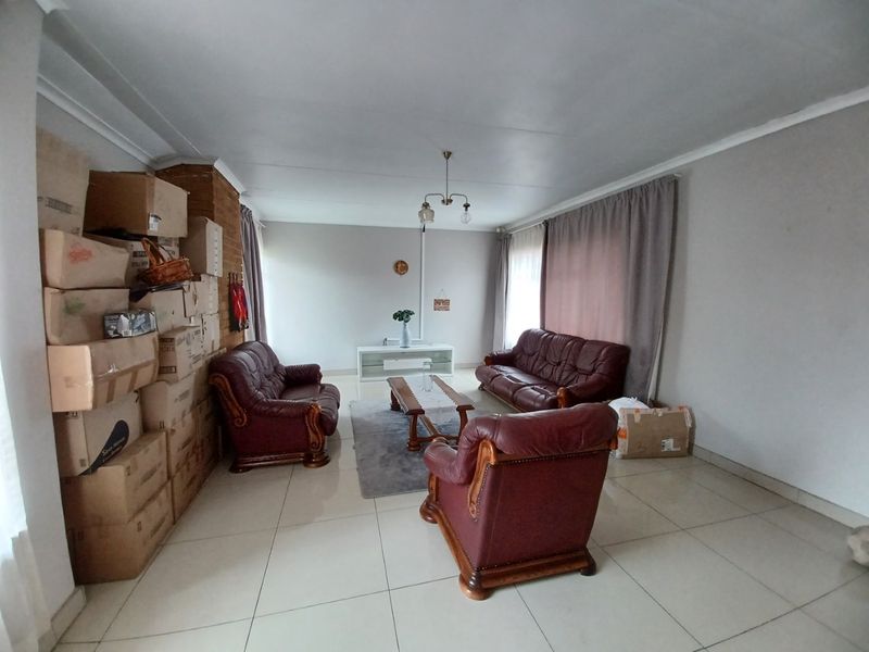 A spacious living room featuring tiled flooring, a brick fireplace, and cove cornicing, offering a neutral base for potential interior updates.