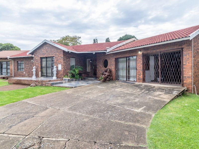 Front view of a single-story face brick house featuring a tiled roof, concrete driveway, and multiple sliding door entrances with security gates.