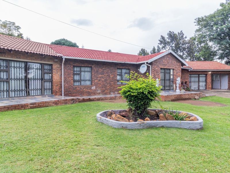 Rear view of a single-story face brick house featuring a tiled roof, paved patio area, and established garden.