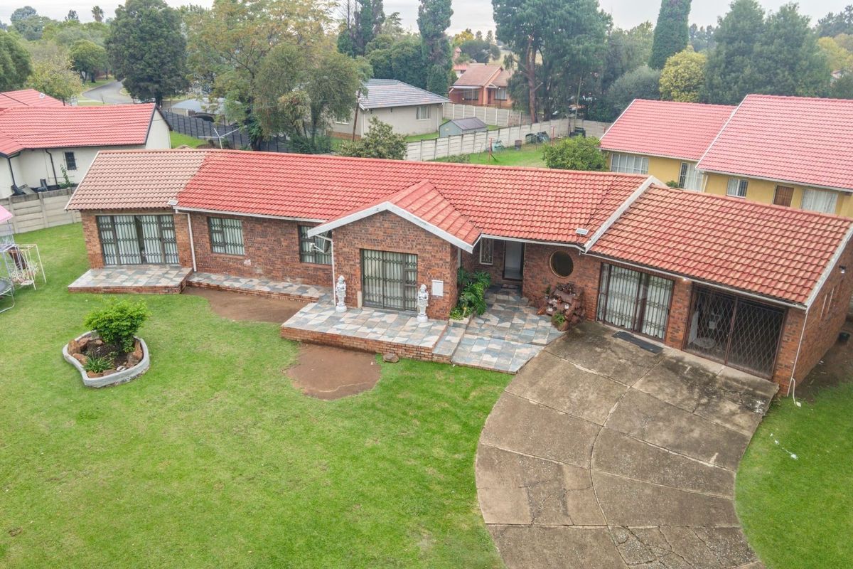 Aerial view of a single-story brick house featuring a tiled roof, paved driveway, and a spacious surrounding lawn.