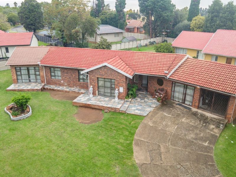 Aerial view of a single-story brick house featuring a tiled roof, paved driveway, and a spacious surrounding lawn.