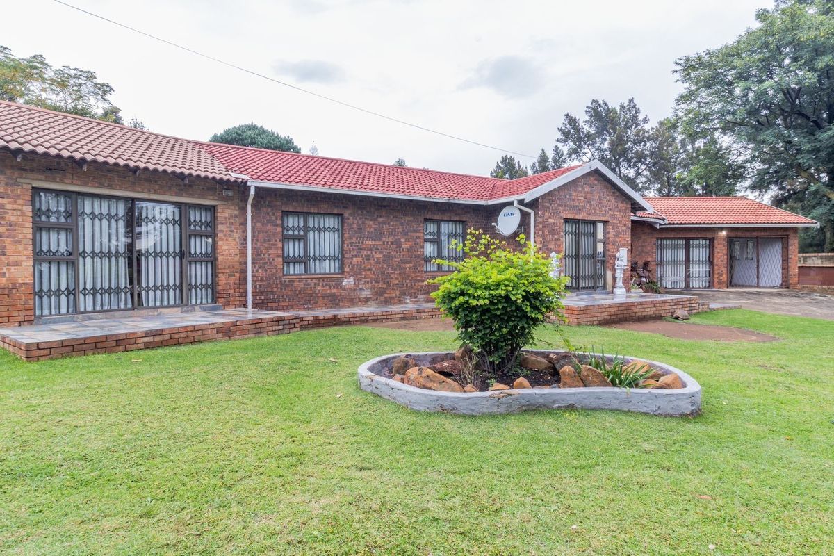 A spacious rear exterior view of a face brick house featuring a tiled roof, paved patio areas, and a well-maintained garden.