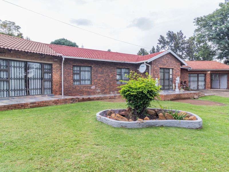 A spacious rear exterior view of a face brick house featuring a tiled roof, paved patio areas, and a well-maintained garden.