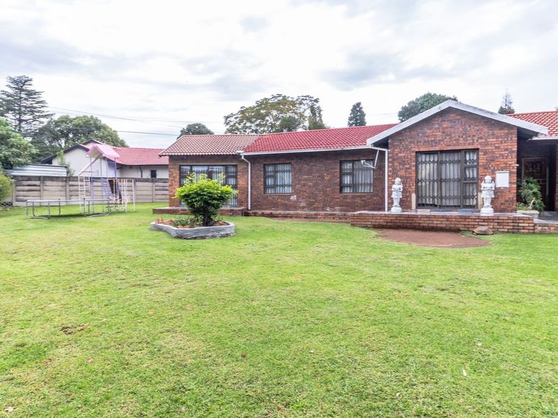Rear view of a face brick house featuring a tiled roof, security gates, and a spacious lawn with a brick patio area.