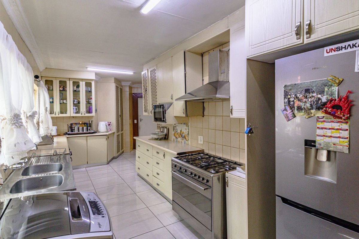 A functional kitchen featuring built-in cabinetry, a stainless steel gas stove with extractor fan, double basin sink, and tiled flooring throughout.