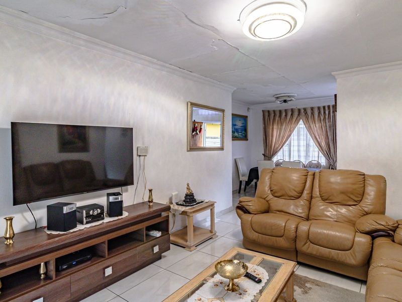 A living room featuring tiled flooring and coved ceilings, showing visible signs of ceiling plaster cracking requiring maintenance.