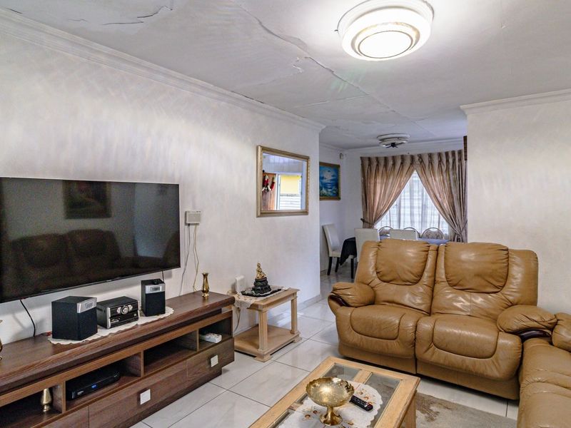 Open plan living and dining area featuring tiled flooring and visible ceiling cracks requiring maintenance.