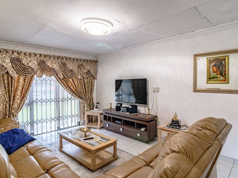 A living room featuring tiled flooring, a sliding glass door with security gate, and a ceiling light fixture. Note visible ceiling cracks.
