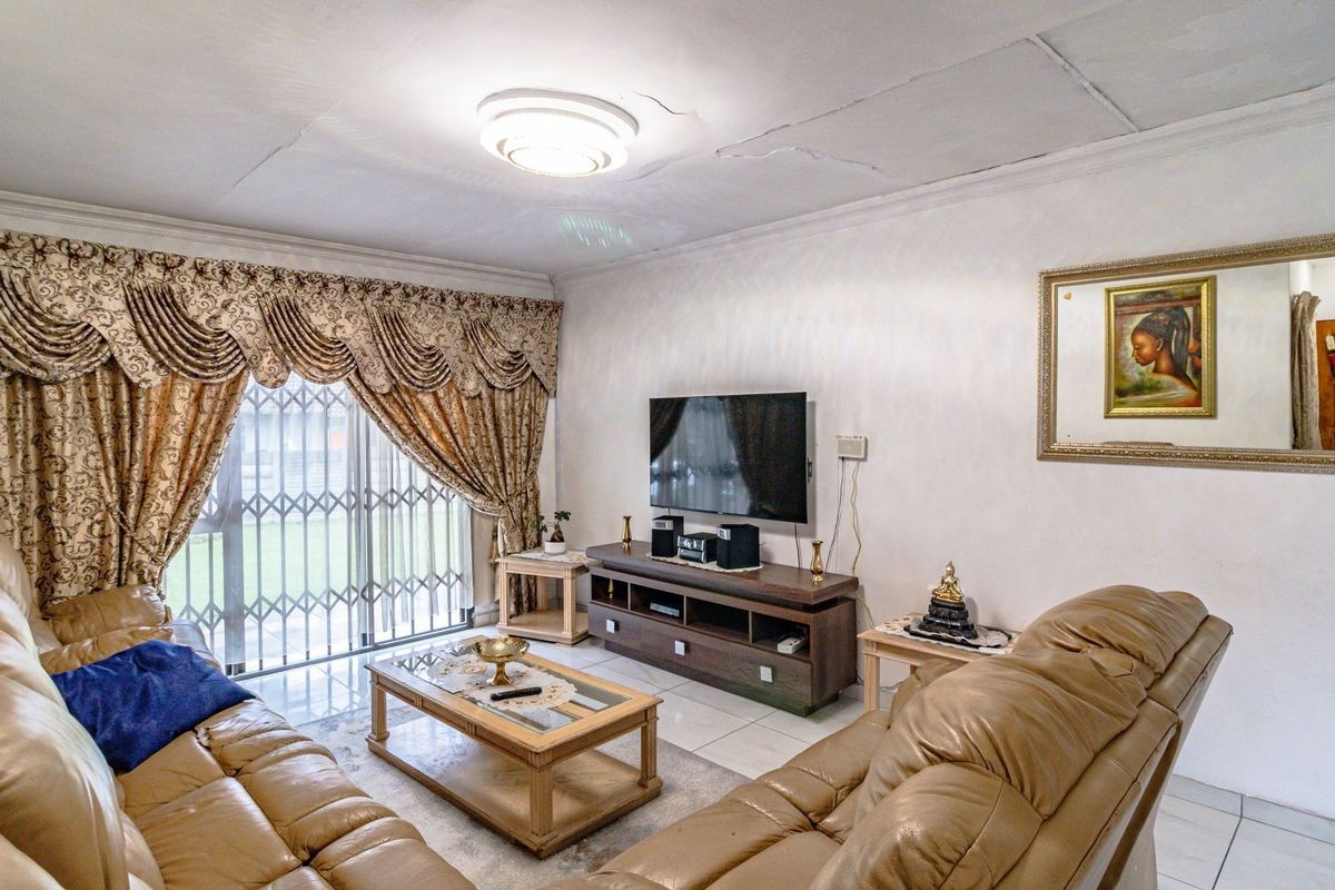 A living room featuring tiled flooring, a sliding glass door with security gate, and a ceiling light fixture. Note visible ceiling cracks.