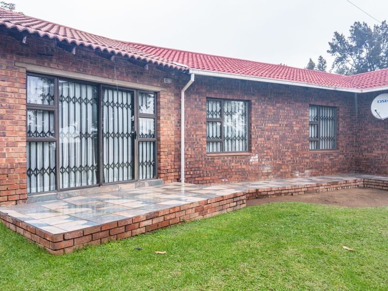 Rear view of a face brick house featuring a tiled patio, sliding glass doors with security gates, and a pitched tiled roof.