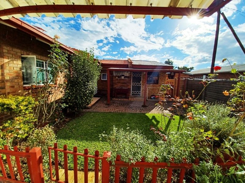 A private rear garden featuring a paved patio area, established lawn, and brick exterior walls under a corrugated metal roof structure.