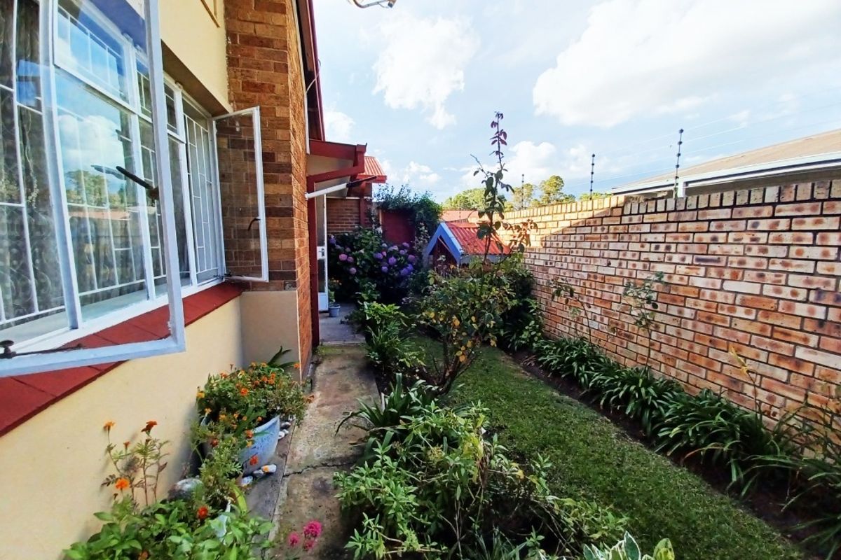 A side garden area featuring a concrete pathway, established garden beds, and a brick boundary wall secured with electric fencing.