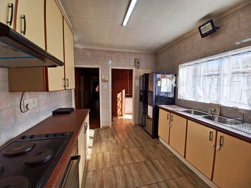 A functional kitchen featuring built-in cabinetry, laminate countertops, an electric hob with extractor, and a double stainless steel sink with tiled finishes.