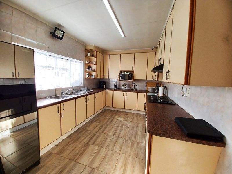 A functional kitchen featuring laminate cabinetry, dark countertops, a double basin sink, built-in oven, microwave, and gas hob with tiled flooring and backsplash.