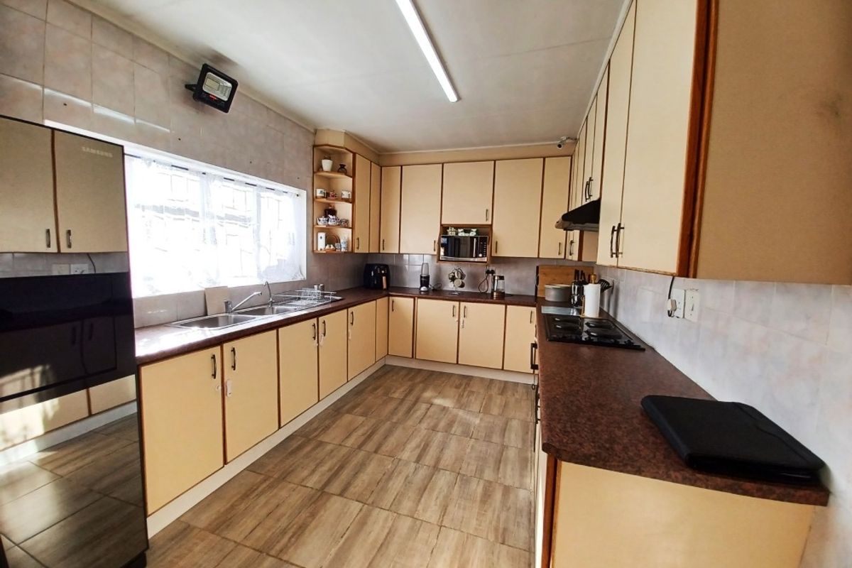 A functional kitchen featuring laminate cabinetry, dark countertops, a double basin sink, built-in oven, microwave, and gas hob with tiled flooring and backsplash.
