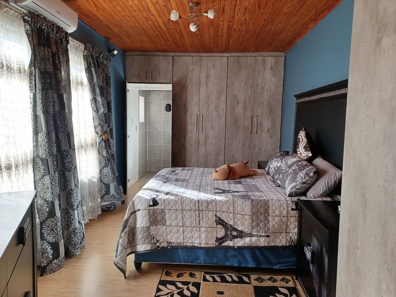 A well-maintained bedroom featuring built-in cupboards, warm wooden ceiling finishes, laminate flooring, and an integrated air conditioning unit with en-suite access.