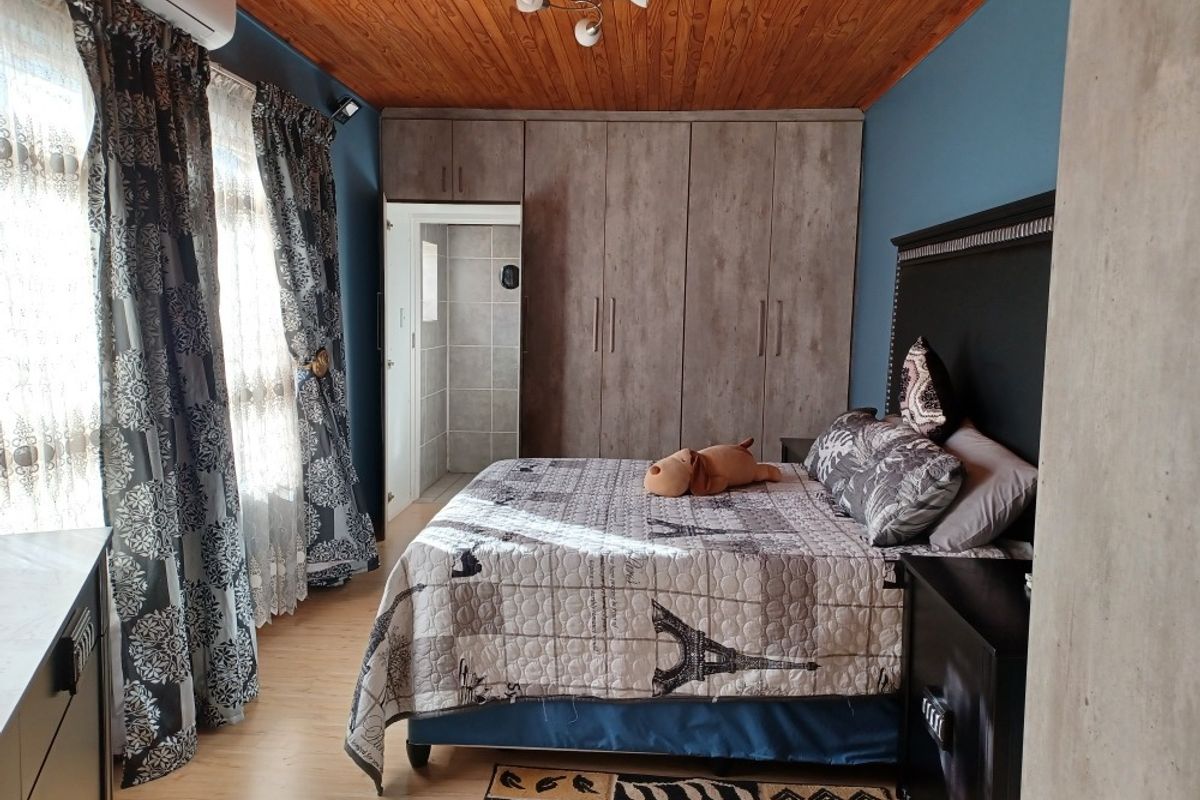 A well-maintained bedroom featuring built-in cupboards, warm wooden ceiling finishes, laminate flooring, and an integrated air conditioning unit with en-suite access.
