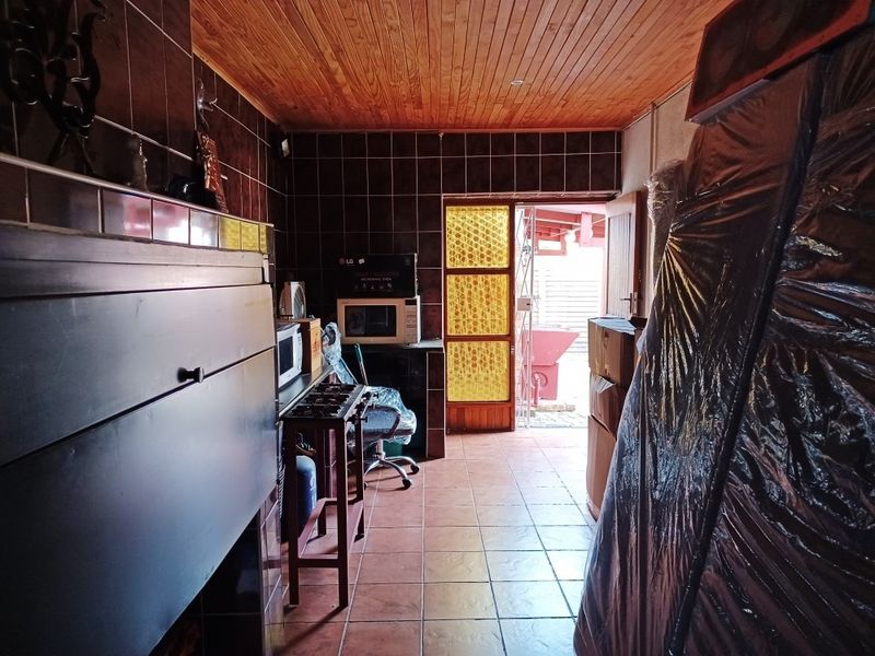 A functional scullery or utility area featuring tiled walls, timber ceiling, and a built-in braai, with direct access to the rear exterior.