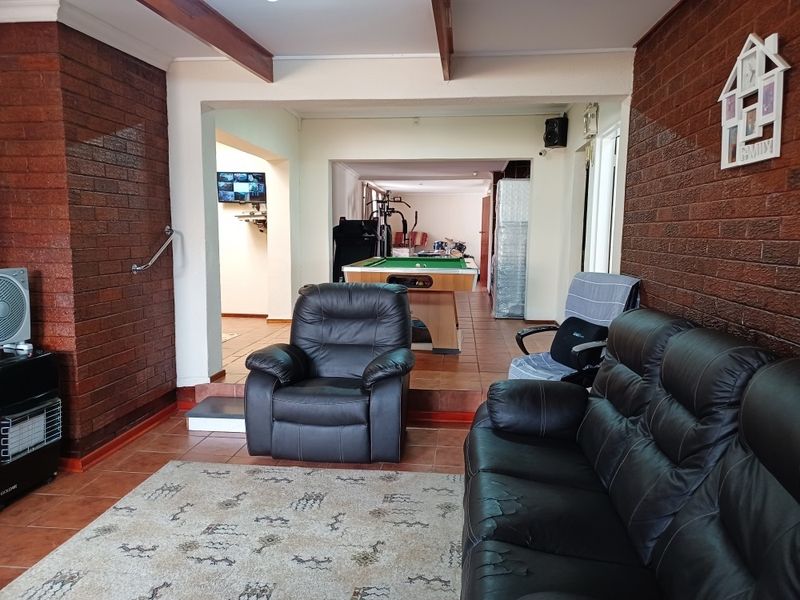 Open plan living area featuring exposed timber ceiling beams, face brick walls, and tiled flooring with a stepped transition between spaces.