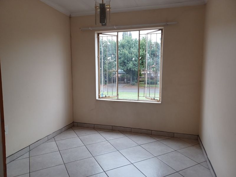 An empty bedroom featuring tiled flooring, a large window with security bars, and neutral wall finishes, ready for personalization.