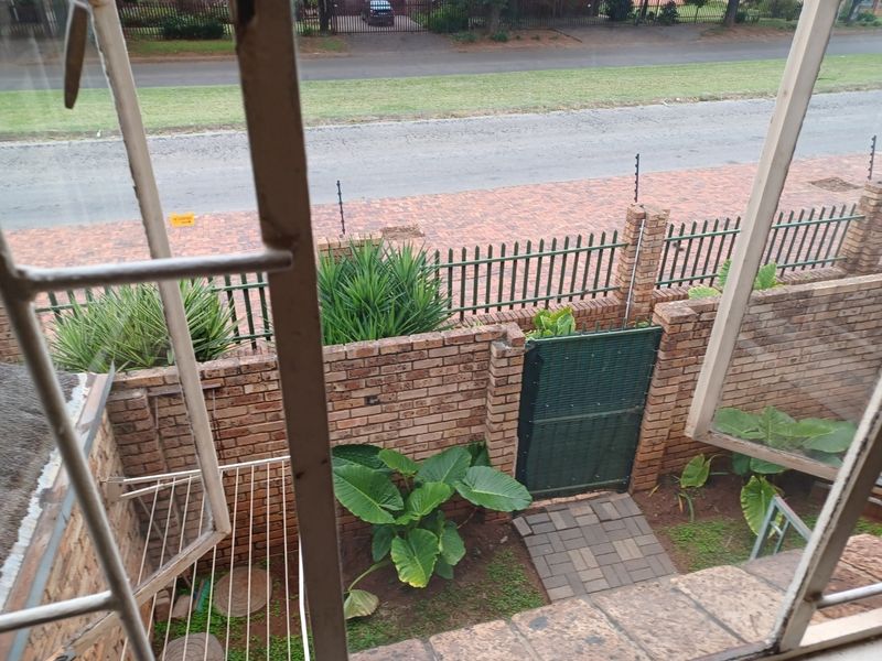 View from an elevated window overlooking a private courtyard with brick boundary walls, a security gate, and paved access path.