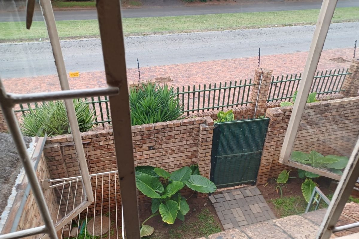 View from an elevated window overlooking a private courtyard with brick boundary walls, a security gate, and paved access path.