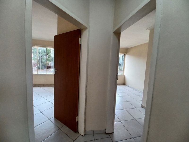 A view from a central hallway looking into two empty bedrooms, featuring tiled flooring and standard internal wooden doors.