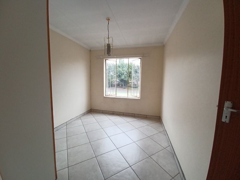 A clean, empty bedroom featuring neutral tiled flooring, a window with security bars, and a central pendant light fixture.