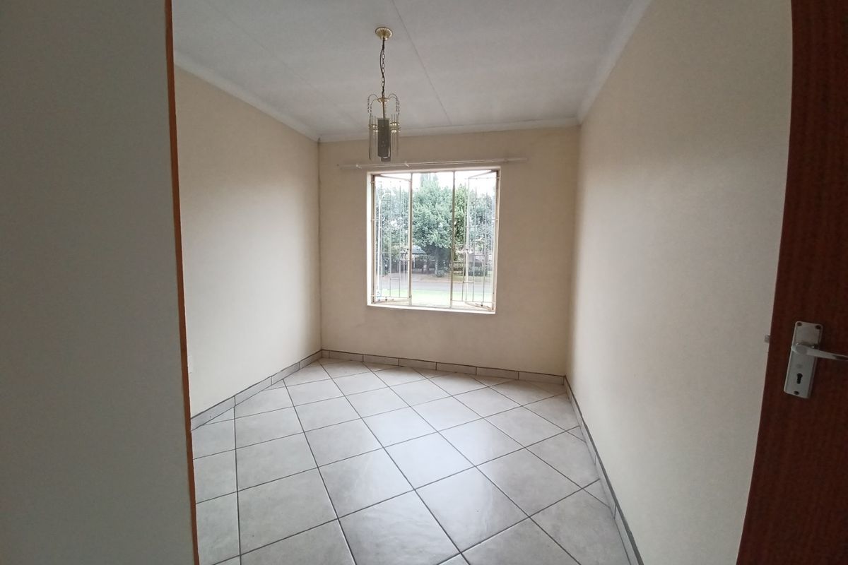 A clean, empty bedroom featuring neutral tiled flooring, a window with security bars, and a central pendant light fixture.