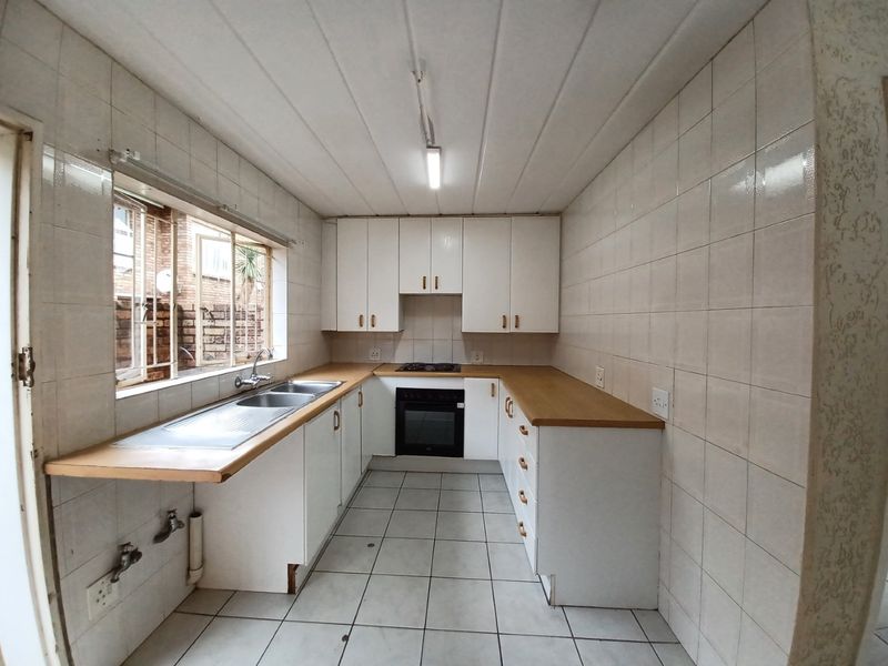 A functional, empty kitchen featuring white built-in cabinetry, laminate countertops, a built-in oven and hob, and fully tiled walls and floors.