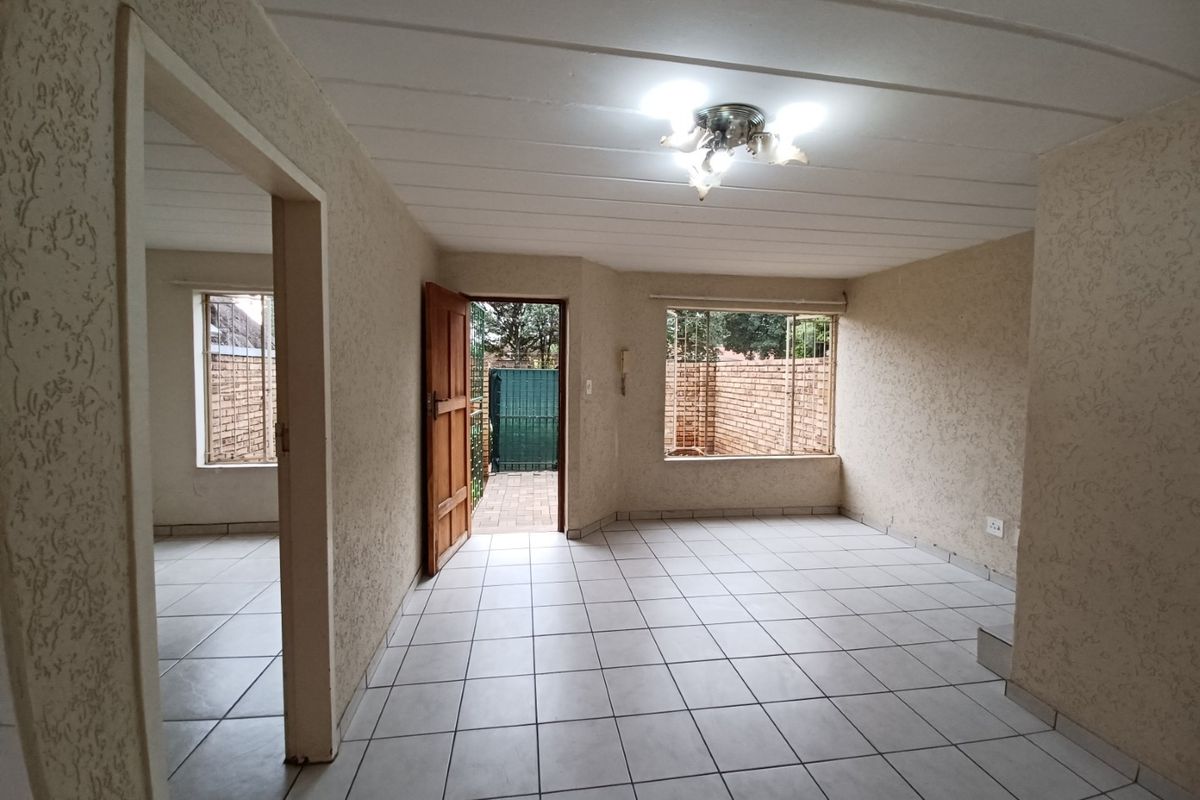 An empty living area featuring tiled floors, textured walls, and direct access to an outdoor space through a timber door.