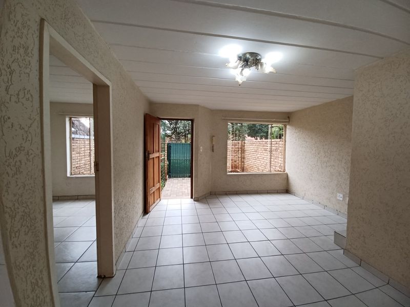 An empty living area featuring tiled floors, textured walls, and direct access to an outdoor space through a timber door.