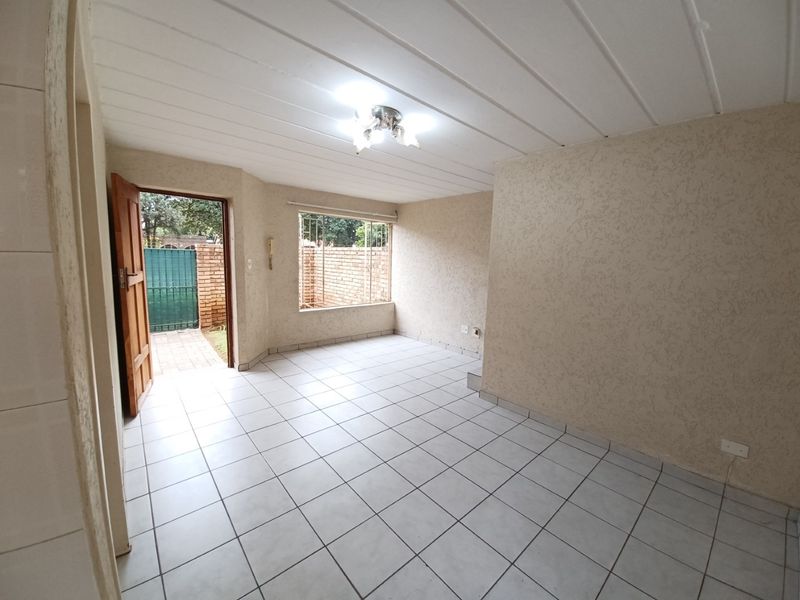 An empty living room featuring tiled flooring, textured walls, and direct access to an outdoor area through a timber door.