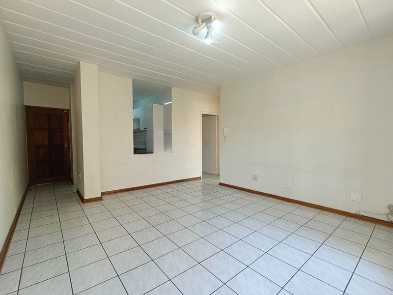 An empty, open-plan living area featuring tiled flooring, a pass-through window to the kitchen, and a neutral interior finish.