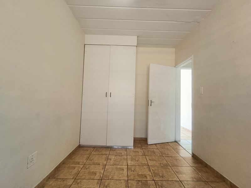 An empty bedroom featuring tiled flooring, a built-in wardrobe, and a panel ceiling, offering a blank canvas for personalization.