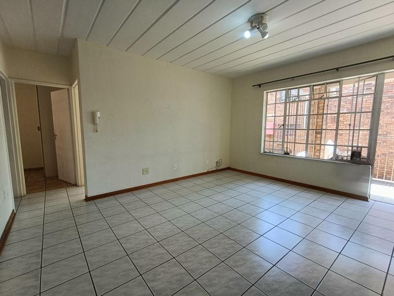 An empty living room featuring tiled flooring, ceiling paneling, and a large window with security bars, offering a blank canvas for renovation.