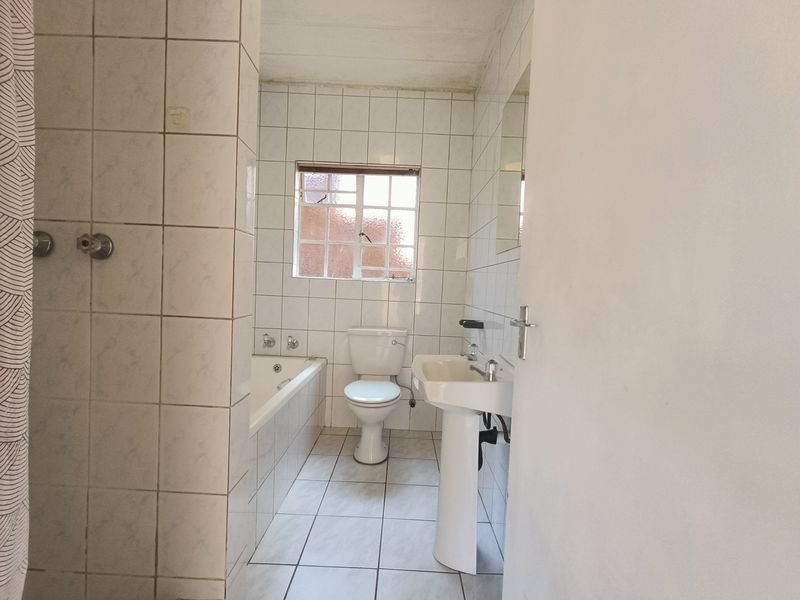 A functional bathroom featuring a pedestal basin, toilet, and bathtub with white wall and floor tiling, requiring some cosmetic updates.