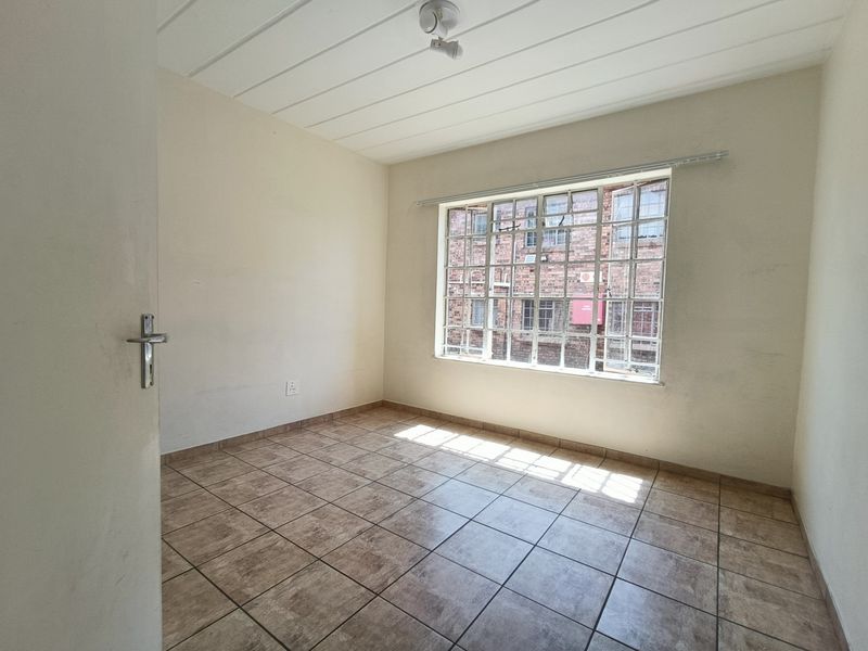 An empty bedroom featuring tiled flooring, a panelled ceiling, and a window fitted with security bars.