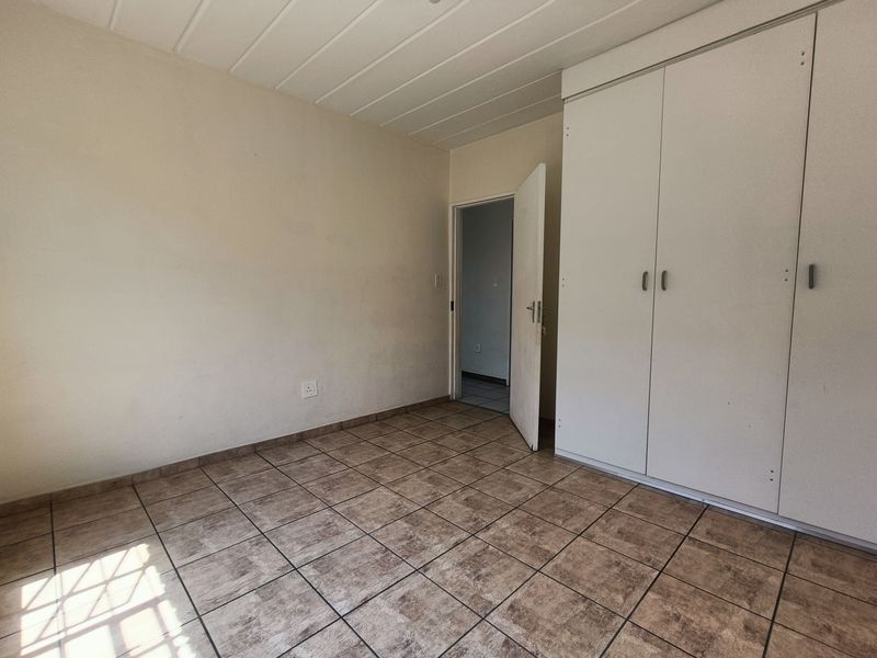 A vacant bedroom featuring tiled flooring, a panelled ceiling, and built-in cupboards, offering a clean and neutral space ready for personalization.