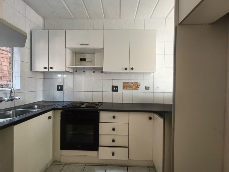 A functional kitchen featuring white cabinetry, dark countertops, a built-in oven and hob, and tiled finishes throughout.