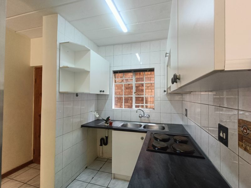 Compact kitchen featuring white cabinetry, dark countertops, an electric hob, and a double basin sink with tiled splashbacks.
